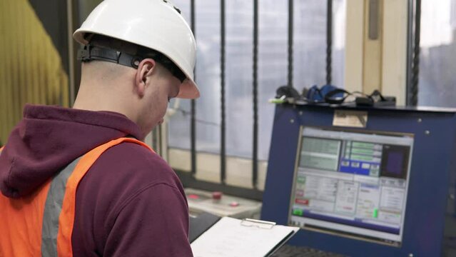 A CNC operator programs a plasma cutting machine in a workshop. An industrial worker enters commands into a computer program to produce metal parts.	