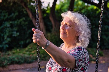 An elderly lady in the park is holding on to the chain of a swing.