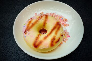 This image is of a single donut on a white plate. Donuts look like this:

- The color of the donut is a soft yellow. It has light brown stripes similar to grilling or burning.
- There are pink bits an