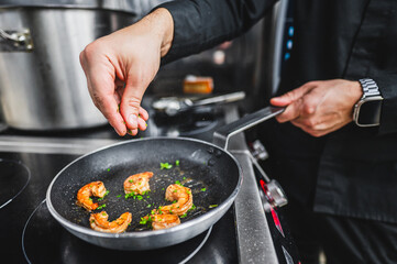 Close-up of a chef’s hand seasoning shrimp in a pan, capturing the action and detail of cooking