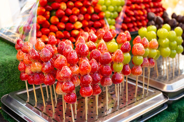 Ripe red strawberries on skewers in sugar syrup. Strawberries in glass. Street food, delicious dessert