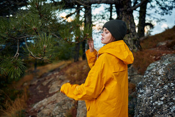 Fototapeta premium A woman in a yellow raincoat enjoying a scenic hike through a peaceful pine forest on a rocky hillside