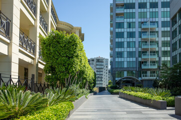 A landscaped urban area with paved walkways, decorated with plants and trees in garden beds,...