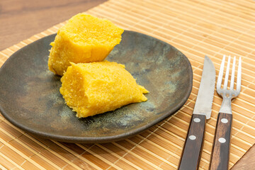 Delicious pieces of steamed cornbread on a rustic plate, set on a bamboo mat with a neatly placed knife and fork.