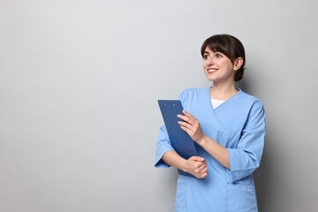 Portrait of smiling medical assistant with clipboard on grey background. Space for text
