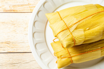 Traditional Brazilian pamonha wrapped in corn husks, presented on a white plate with a rustic...