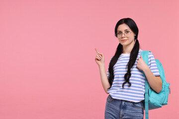 Student with backpack pointing at something on pink background. Space for text
