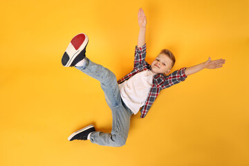 Happy little boy dancing on yellow background, top view