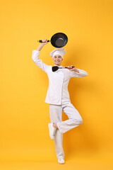 Professional chef with wok and spatula having fun on yellow background