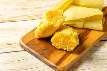 Traditional Brazilian pamonha served on a rustic wooden board, showcasing its vibrant yellow color and authentic texture.