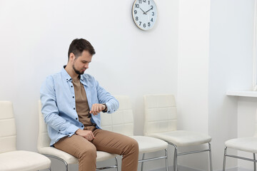 Man looking at wrist watch and waiting for appointment indoors