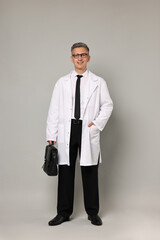 Doctor in glasses holding briefcase on grey background