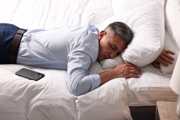 Businessman in office clothes sleeping on bed indoors