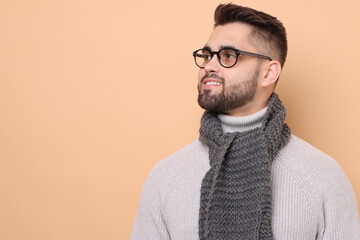 Obraz premium Smiling man in knitted scarf on beige background. Space for text