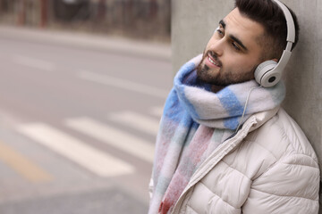 Smiling man in warm scarf and headphones on city street. Space for text