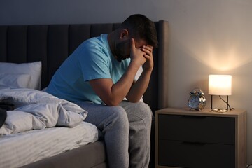 Fototapeta premium Man covering face with hands on bed indoors
