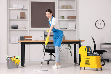 Cleaning service worker washing floor with mop. Bucket with supplies and wet floor sign in office