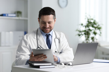 Smiling doctor having online consultation via tablet at table in clinic