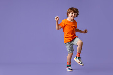 Happy little boy dancing on violet background. Space for text