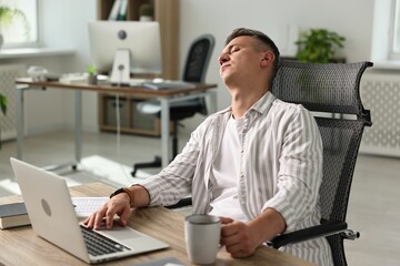 Man with cup of drink snoozing at wooden table in office