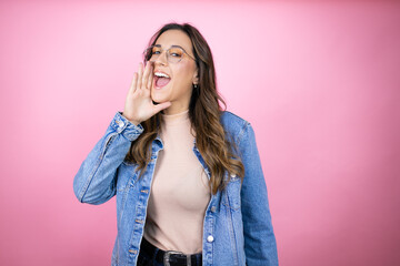 Young beautiful woman wearing denim jacket over isolated pink background shouting and screaming loud to side with hand on mouth