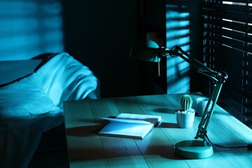 Stylish lamp and open book on wooden table at night