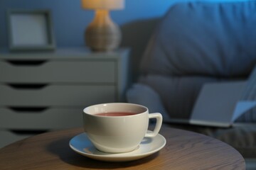 Cup of hot tea on wooden table at night
