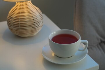 Cup of hot tea and nightlight on white table at night