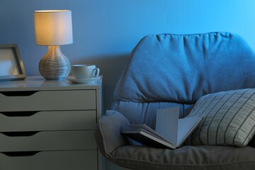 Comfortable armchair and white chest of drawers in room at night