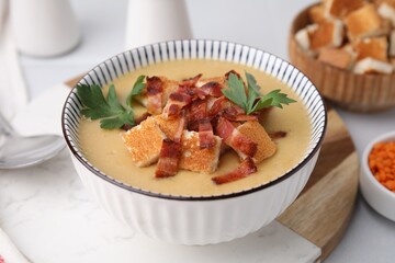 Delicious lentil soup with bacon and parsley in bowl on table, closeup