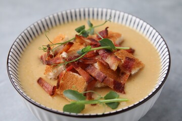 Delicious lentil soup with bacon and microgreens in bowl on gray table, closeup
