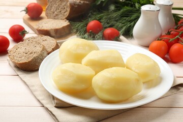 Plate with young boiled potatoes on light wooden table, closeup