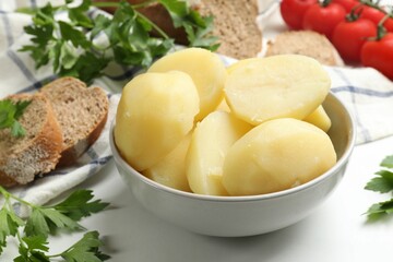 Young boiled potatoes in bowl, bread and parsley on white table, closeup