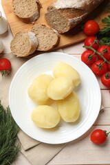 Plate with young boiled potatoes and products on light wooden table, flat lay