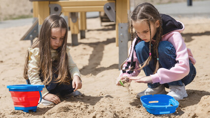 Two little girls sisters playing in sand on playground.