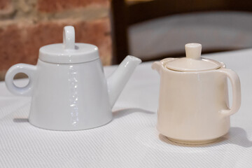 Two teapots on table with brick wall background