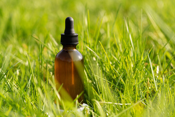 brown serum bottle lying in lush green grass, sunlight reflecting on the bottle