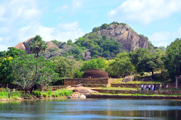 Natural setting of ancient ruins, water body, tropical vegetation and a rock mountain as a backdrop