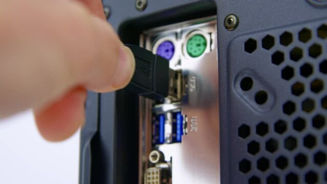 Caucasian male hand pushes a USB plug into the socket on a desktop PC motherboard.