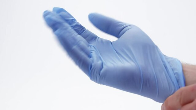 Caucasian male hand in a blue latex surgical glove bends fingers to achieve a better fit, filmed against a white background.
