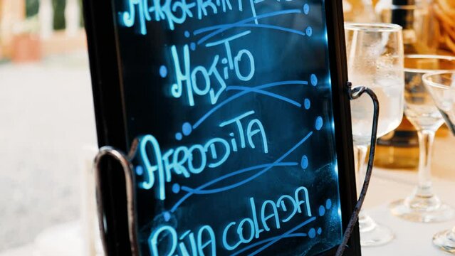 LED sign with handwritten bar cocktail menu water mirror illuminated with blue led light decorated with tropical flowers