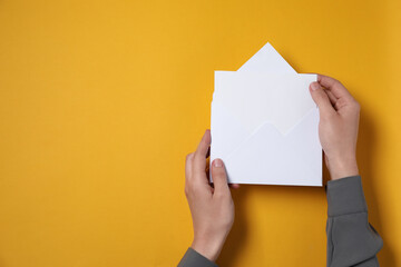 Woman taking card out of letter envelope at orange table, top view. Space for text