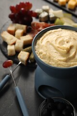 Fondue with tasty melted cheese, forks and different snacks on black table
