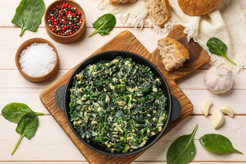 Tasty spinach dip with eggs in dish served on light wooden table, flat lay