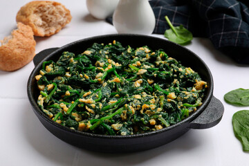 Tasty spinach dip with eggs in dish served on white tiled table, closeup