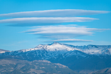 Huge lenticular clouds over the snowy peaks of the Sierra Nevada in Granada (Spain) at sunset