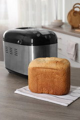 Breadmaker and fresh homemade bread on wooden table in kitchen