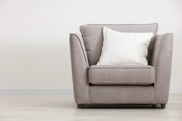 Soft white pillow on armchair near light wall indoors, space for text