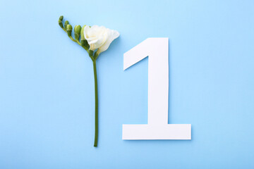 Paper number 1 and beautiful flower on light blue background, top view