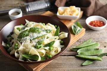 Delicious pasta with green peas, fresh basil and cheese on wooden table, closeup